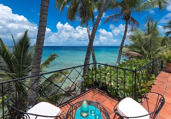 Une terrasse offrant une vue sur l’océan, entourée de palmiers et agrémentée d’une balustrade.