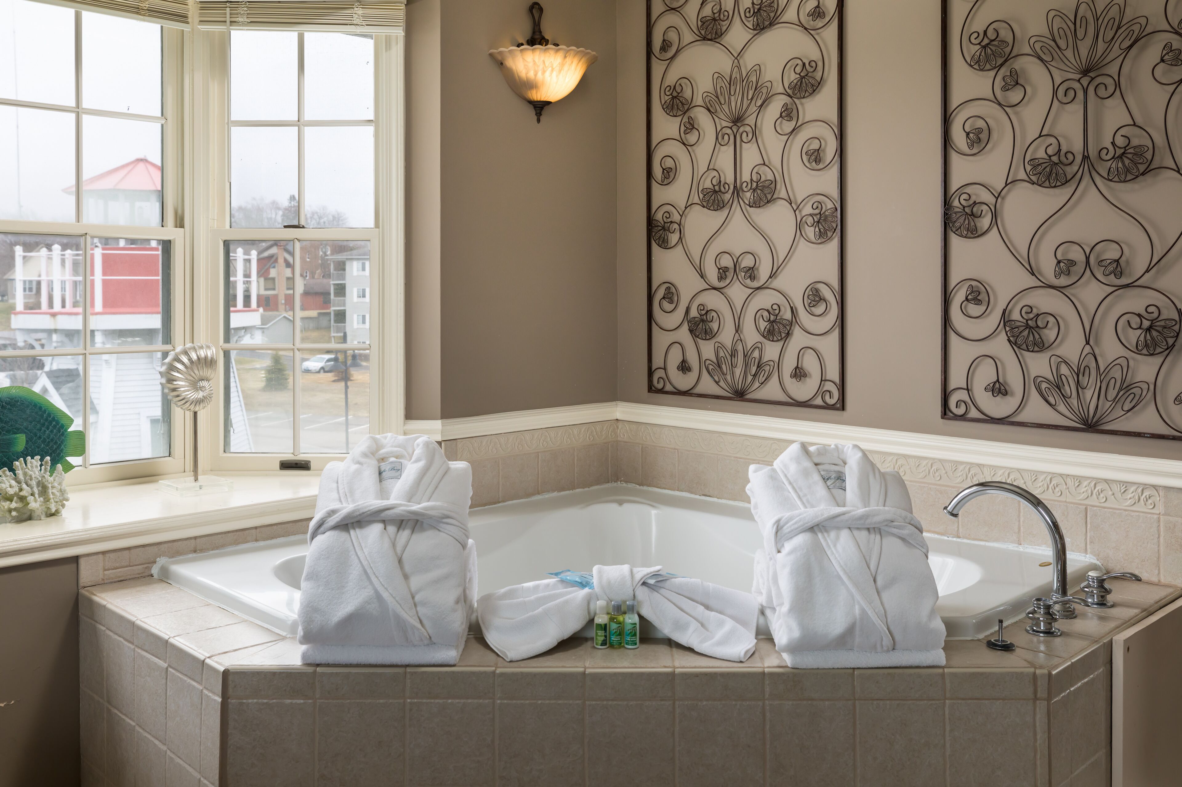 A bathroom with a large bathtub, a window with a view of buildings, and a decorative wall panel.