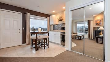A modern kitchen with a bar area, a dining table with stools, and a view of the city through large windows.