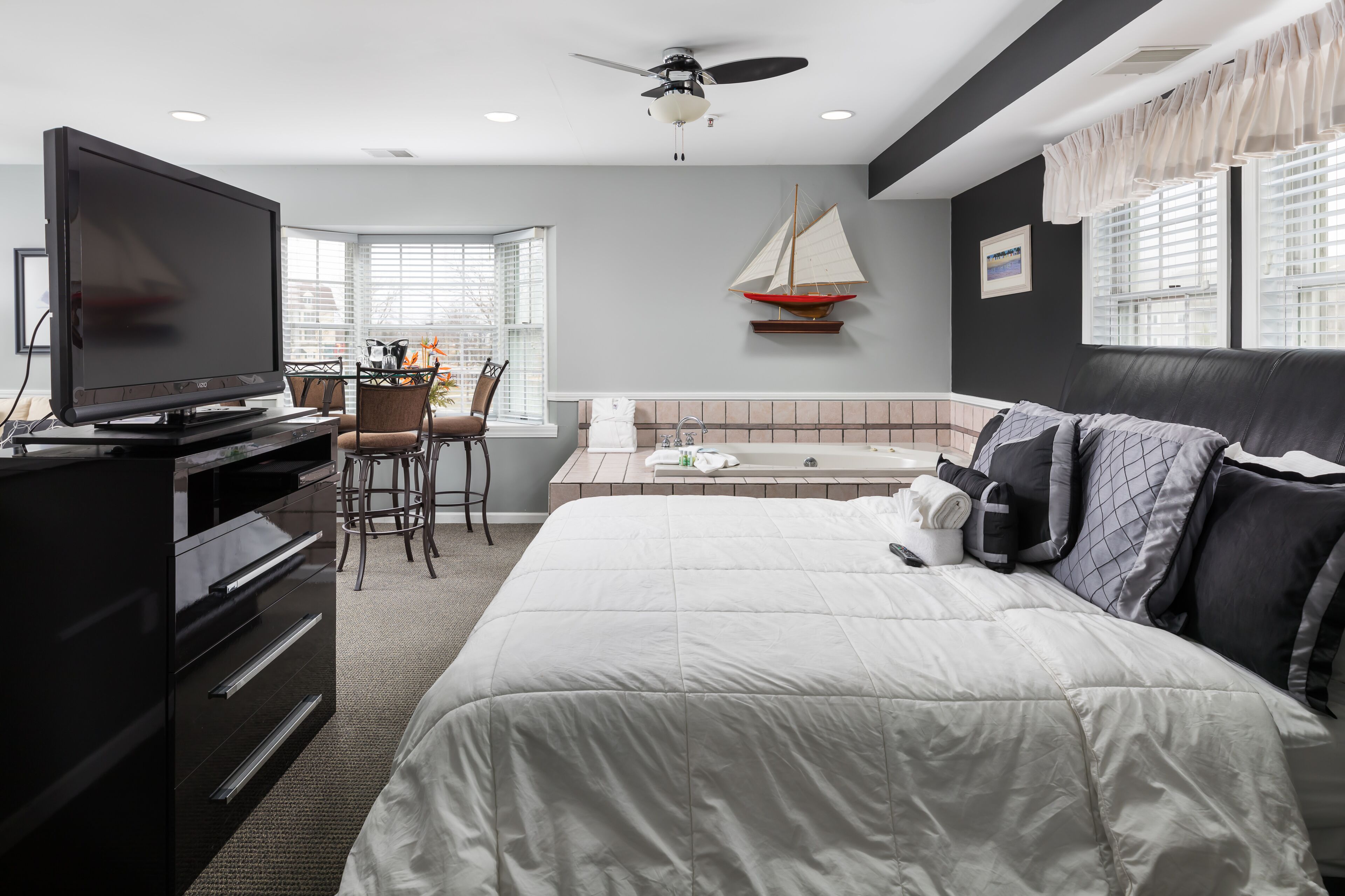 A hotel room with a bed, a TV, a desk with a chair, a small sailboat decoration, and a bathtub.