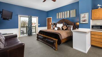 A bedroom with a large bed, a ceiling fan, a TV, and a sliding glass door leading to a balcony.
