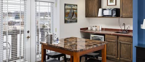 A kitchen with a granite countertop, wooden cabinets, and a microwave. There is a painting of a sailboat on the wall.