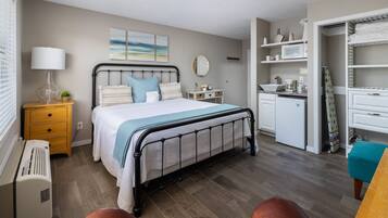 A bedroom with a bed, bedside table, lamp, and a small plant. There is a bathroom with a sink, mirror, and towel rack.