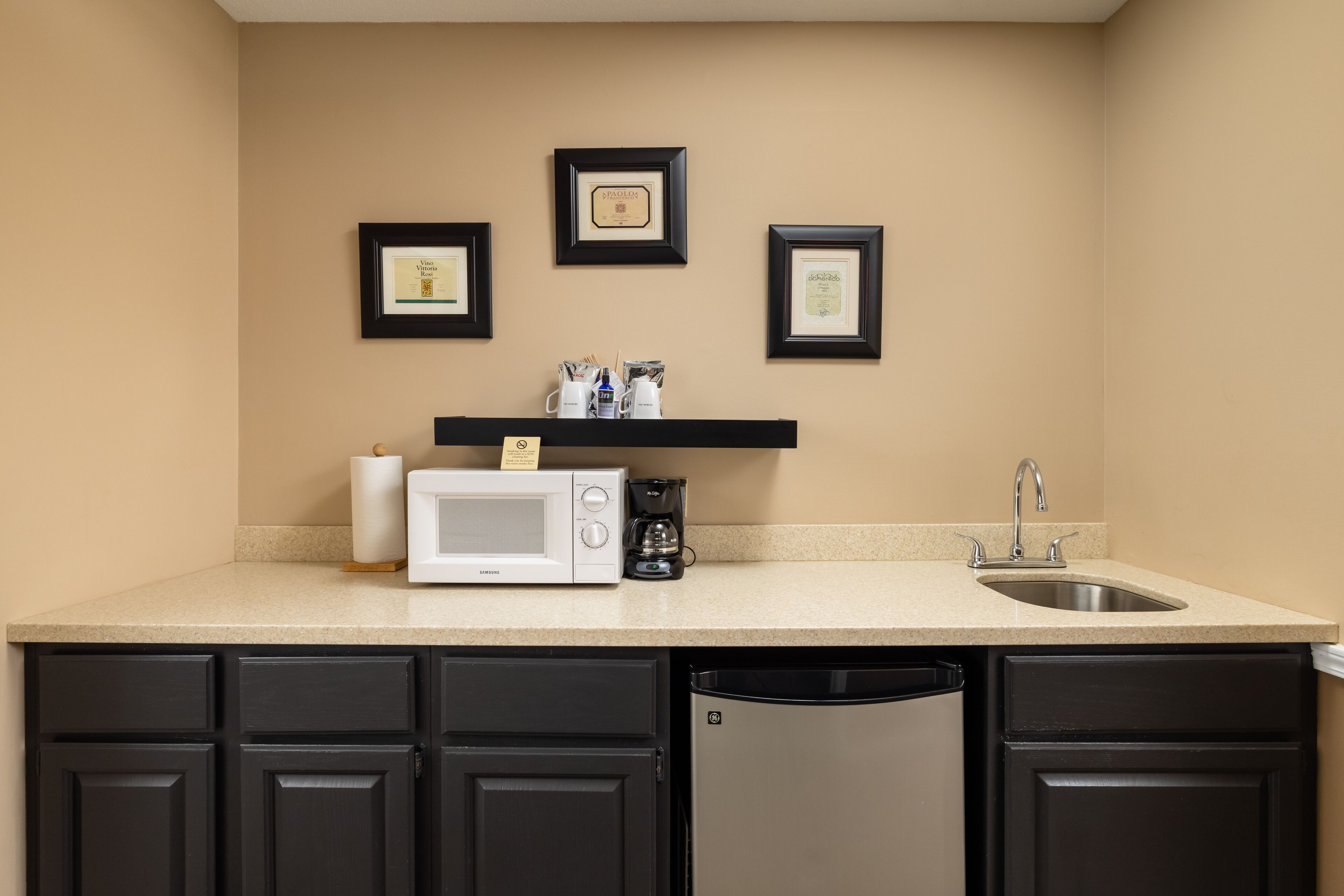 A kitchen with a microwave, coffee maker, and sink. There are framed certificates on the wall.