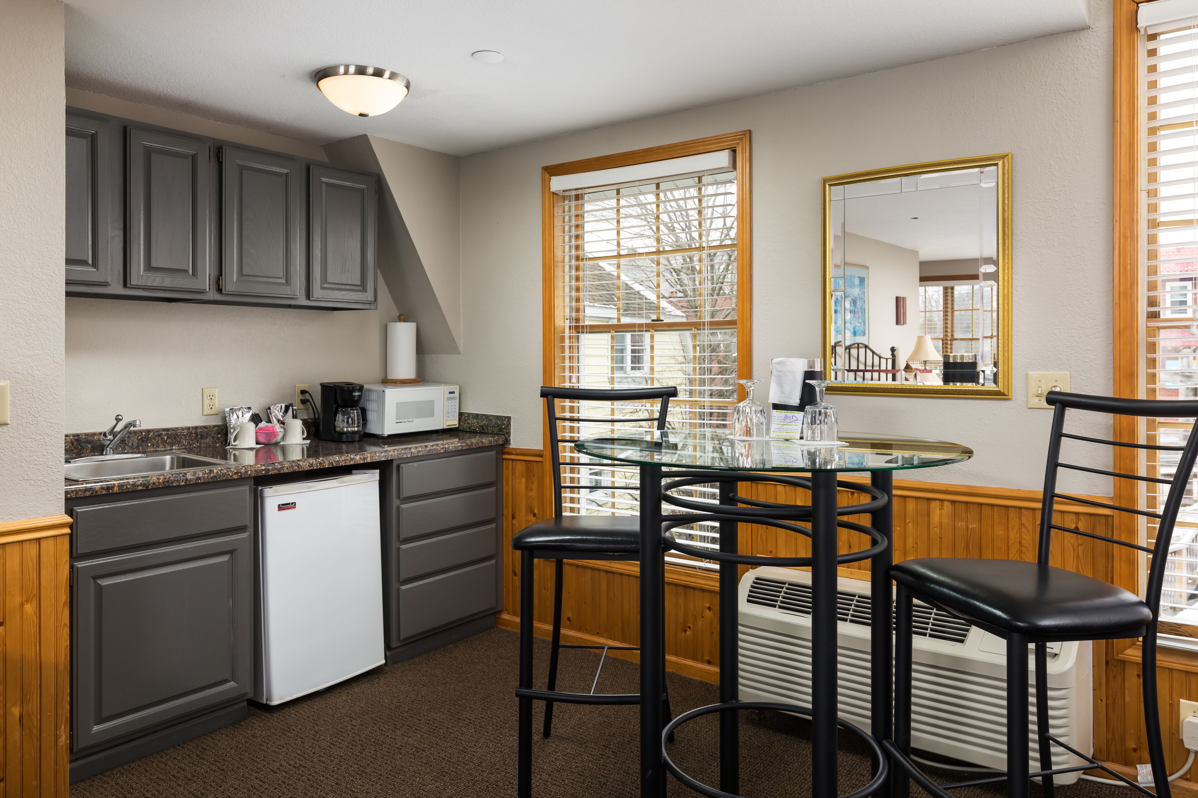 A compact kitchen with a refrigerator, microwave, and a glass table with chairs.