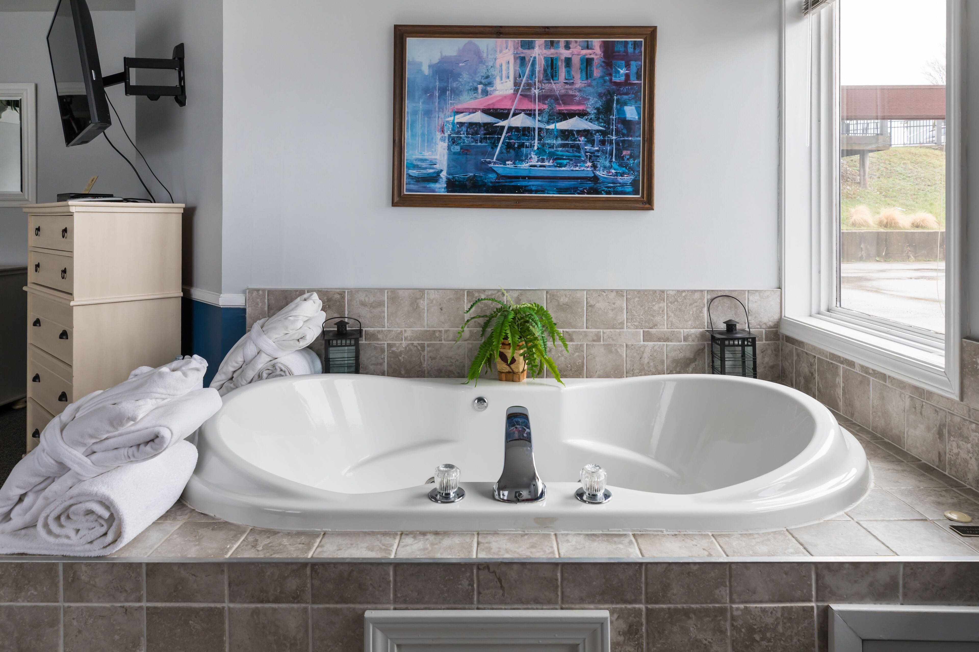 A modern bathroom with a freestanding bathtub, a potted plant, and a framed painting above the tub.