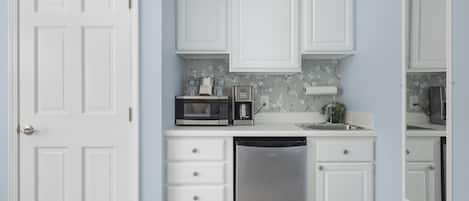 A compact kitchen with white cabinetry, a dishwasher, a microwave, and a coffee maker.