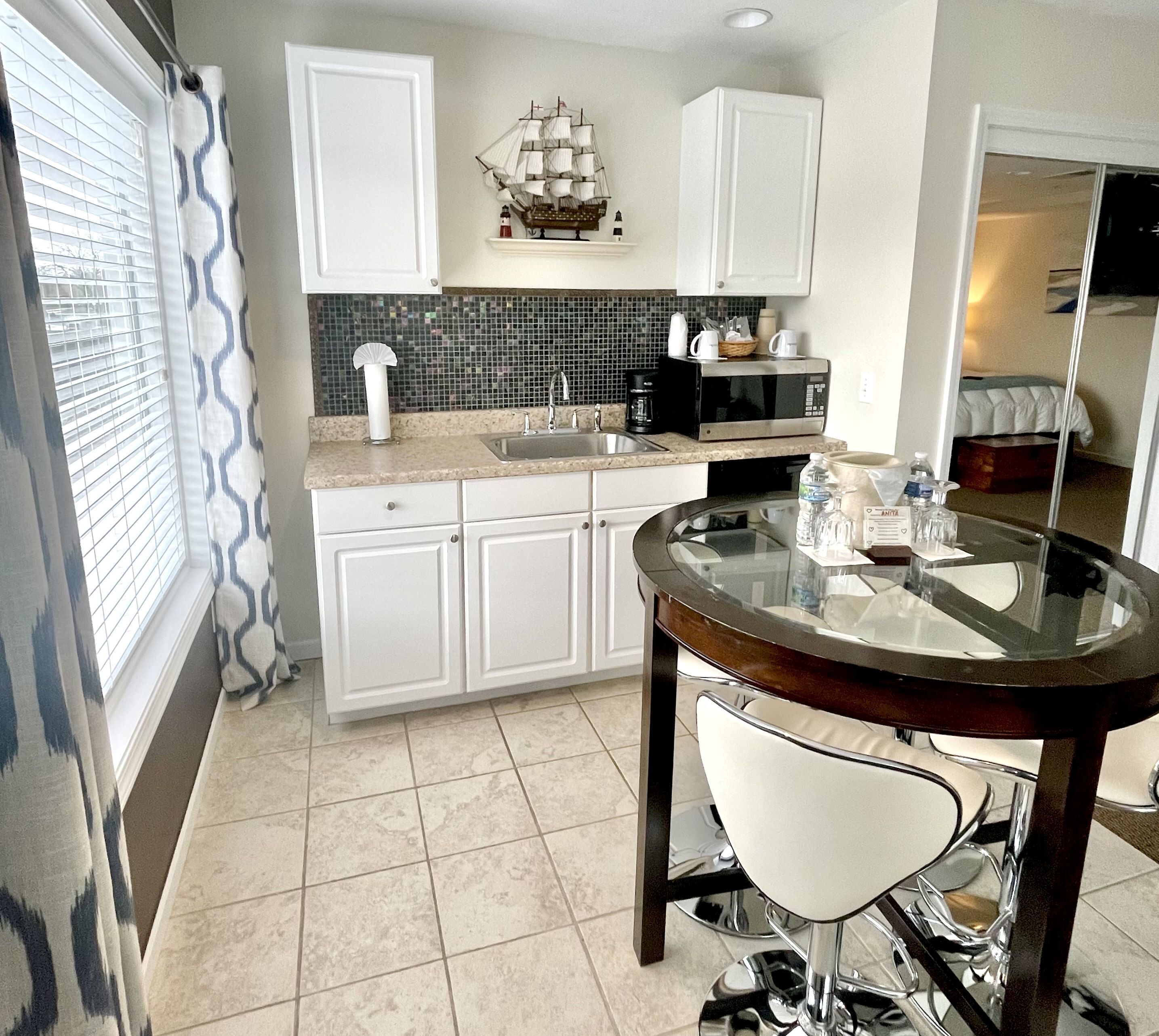 A modern kitchen with white cabinets, a black microwave, a sink, and a decorative ship model above the counter.