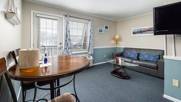 Una sala de estar con una mesa de comedor, sillas, un sofá, un televisor y una ventana con cortinas.