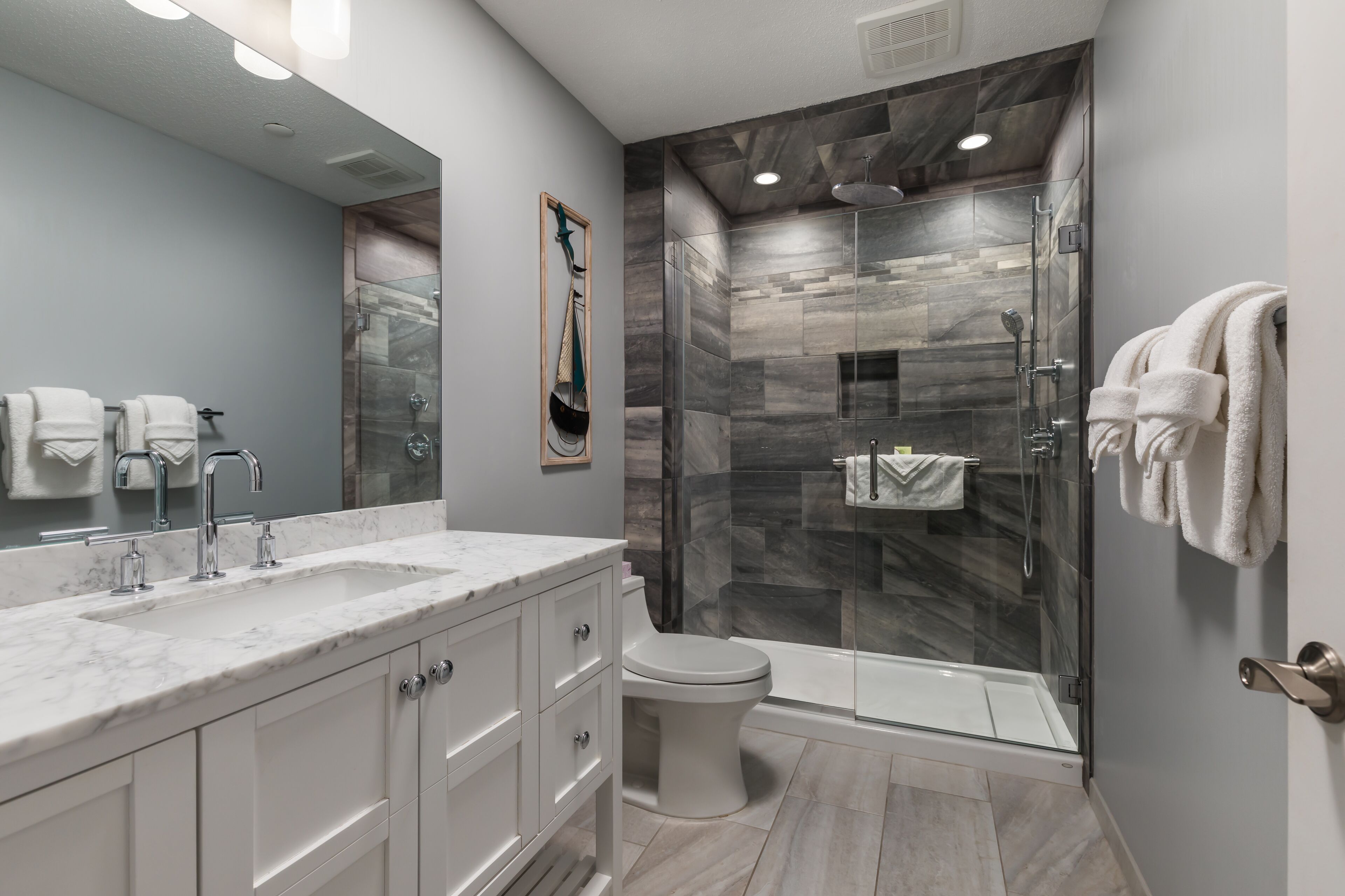 A modern bathroom with a marble sink, a glass shower enclosure, and a toilet.