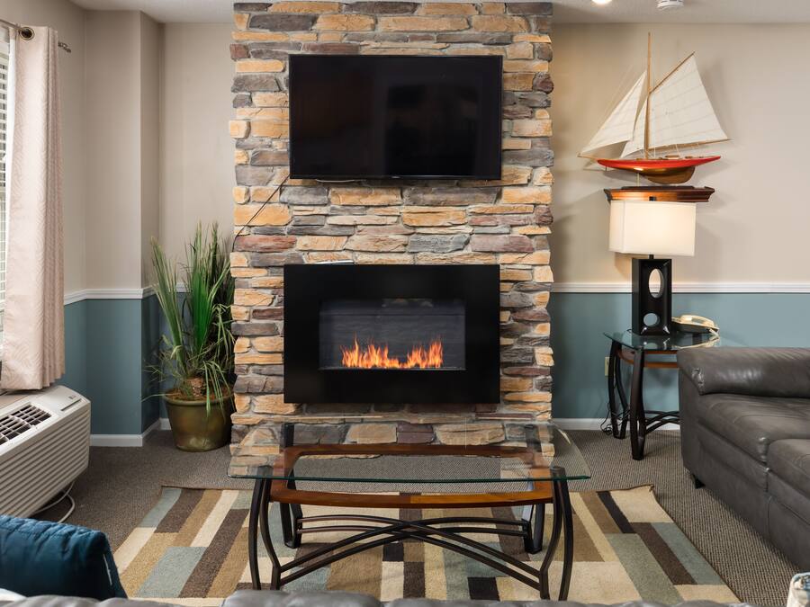 A living room with a stone fireplace, a flat-screen TV above it, and a sailboat decoration on the wall.