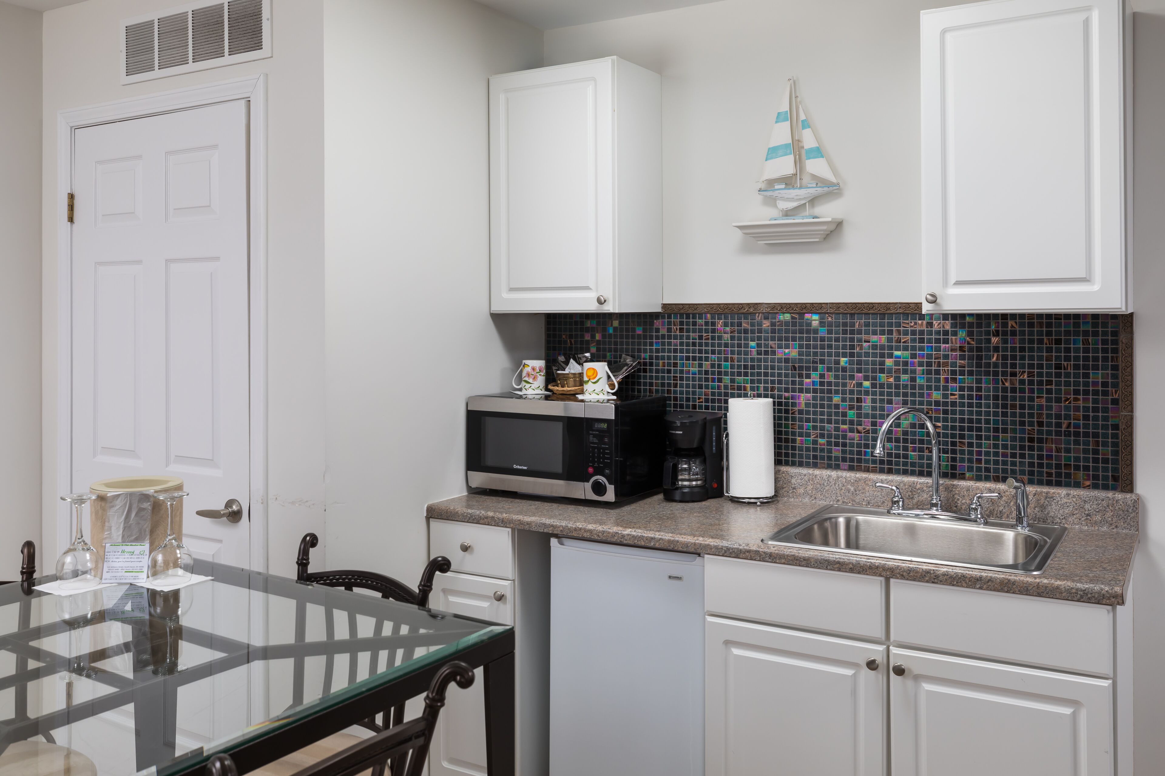 Una cocina compacta con armarios blancos, microondas, cafetera y lavabo.