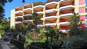 A multi-story hotel with balconies, surrounded by lush greenery and a stone pathway. - APART HOLIDAYS Residenza Flora (Muralto)