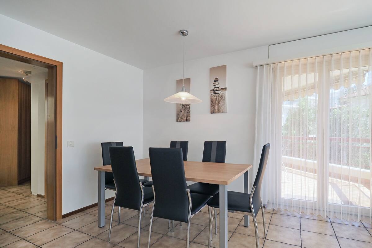 A dining area with a wooden table and black chairs, a pendant light, and artwork on the wall.