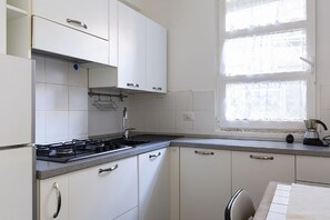 Cocina con armarios blancos, estufa a gas, ventana con vistas y una encimera con un hervidor.
