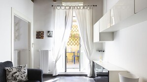 Une chambre moderne avec un canapé, une petite table, un meuble blanc et une vue sur l’extérieur, visible à travers une fenêtre ornée de rideaux.