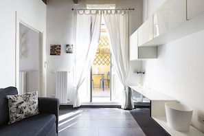 Une chambre moderne avec un canapé, une petite table, un meuble blanc et une vue sur l’extérieur, visible à travers une fenêtre ornée de rideaux.