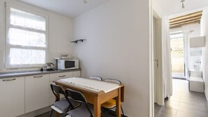 Een kleine keuken met een eettafel, stoelen, een magnetron en een raam met gordijnen.