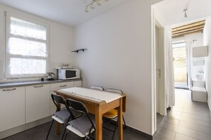 Eine kleine Küche mit Esstisch, Stühlen, einer Mikrowelle und einem Fenster mit Vorhängen.