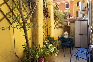 Eine kleine Außenveranda mit einer gelben Wand, einer Holzleiter, einem Tisch mit blauen Stühlen und einem Blumentopf mit Blumen.