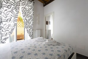 Un dormitorio con cama, ventana con cortinas, espejo y radiador.