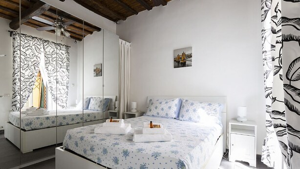 Een slaapkamer met een garderobe met spiegel, een bed met bloemenbedrukking, een nachtkastje en een bijzettafeltje.