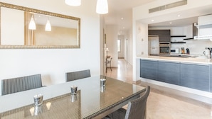 Een moderne keuken met een centraal eiland, een eethoek met een glazen tafel en een grote spiegel aan de muur.