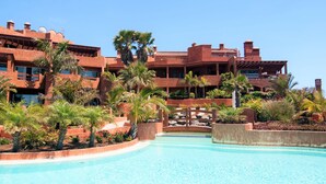 Een resort met een zwembad, palmbomen en een meerlaags gebouw met balkons.