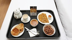 A tray with a teapot, cups, a bowl of soup, a plate of flatbread, a bowl of beans, and a menu. - Hotel Grandeur (Mumbai)