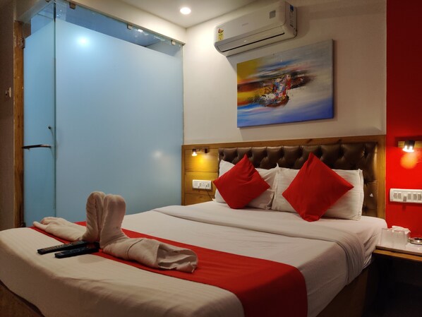 A hotel room with a bed, red pillows, a painting on the wall, and a red and white bedspread.