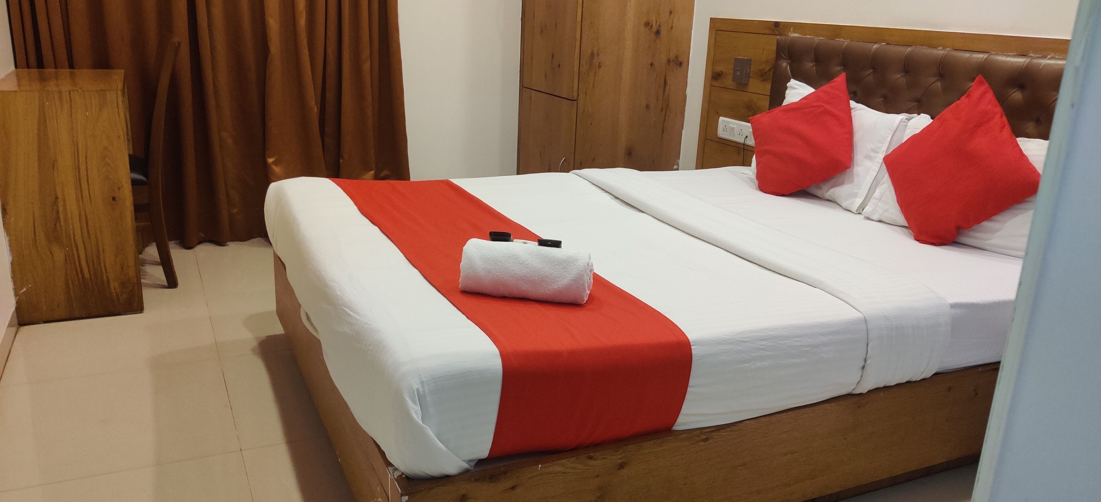 A neatly made bed with a red and white bedspread, a white pillow, and two red pillows.