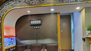 A reception area with a fish tank, two brown armchairs, a glass table with two shot glasses, and a wall clock. - Hotel Grandeur (Mumbai)