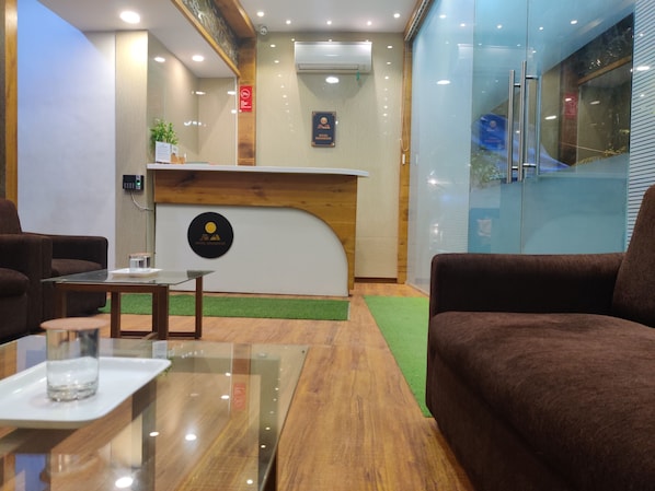 A hotel reception area with a wooden reception desk, a glass coffee table, and brown sofas.