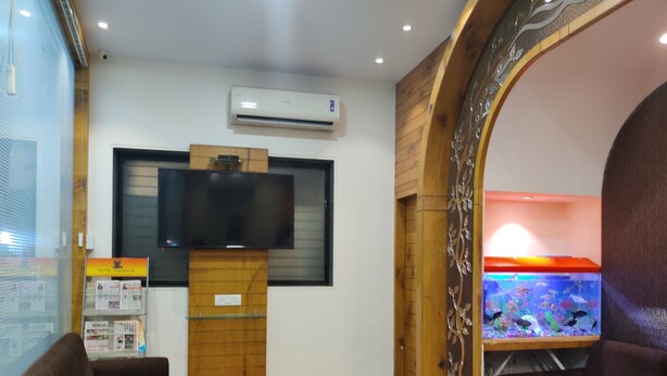 A hotel room with a wooden floor, a flat-screen TV mounted on a wooden stand, a glass coffee table, two brown sofas, and a fish tank with colorful fish. - Hotel Grandeur (Mumbai)