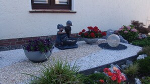 Un jardin agrémenté d’une statue représentant deux enfants, d’une grande sphère décorative et de différents parterres de fleurs.