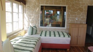 Une chambre avec un mur en pierre, une grande fenêtre, un lit avec une literie à rayures et une armoire en bois.