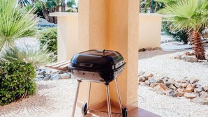 Una parrilla portátil en un patio con palmeras y un cielo despejado al fondo.