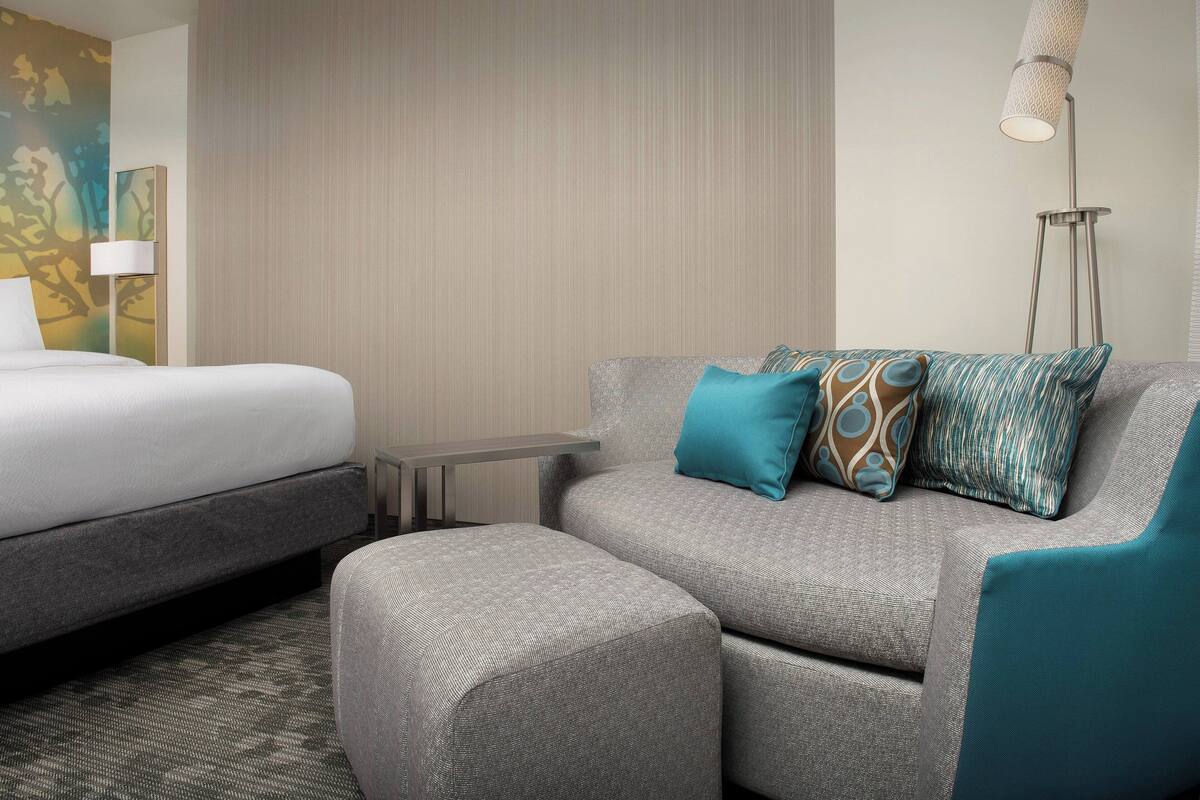 A hotel room with a bed, a sofa, a small table, and a floor lamp.