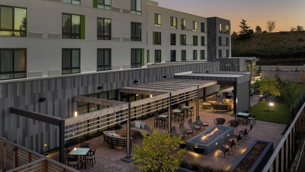 A modern hotel courtyard with outdoor seating, a fire pit, and a view of the building's exterior. - Courtyard by Marriott Portland East (Portland)