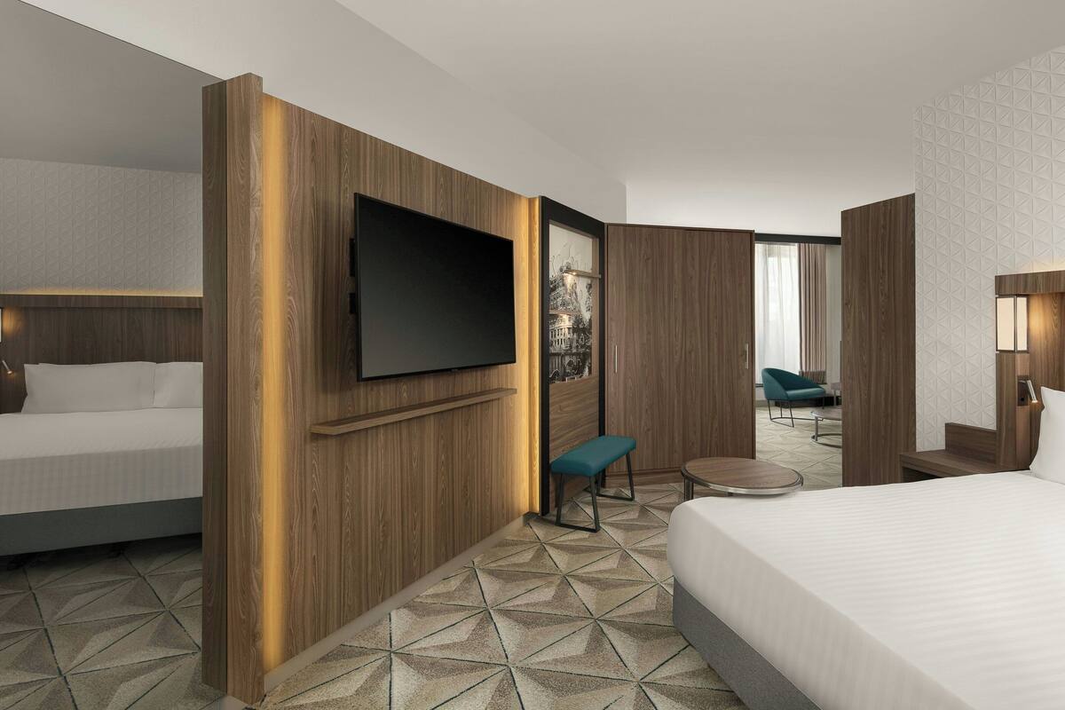 Een moderne hotelkamer met een groot bed, een aan een houten paneel bevestigde televisie, een bankje en een kleine ronde tafel.