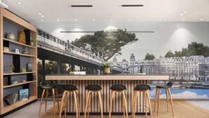 Ein moderner Barbereich mit hölzernen Barhocker und einer Wandmalerei einer Stadtansicht.