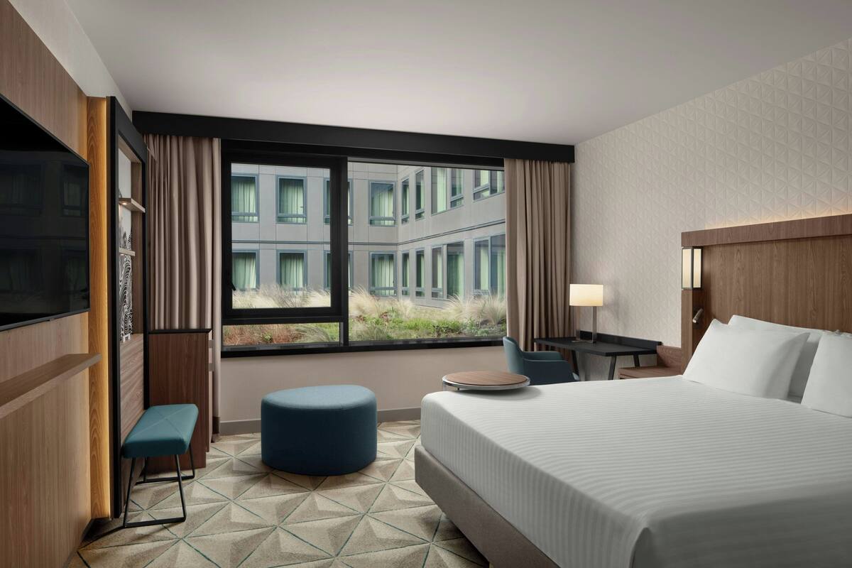 Hotelkamer met een groot bed, een bureau, een stoel, een televisie en een raam met uitzicht op gebouwen.