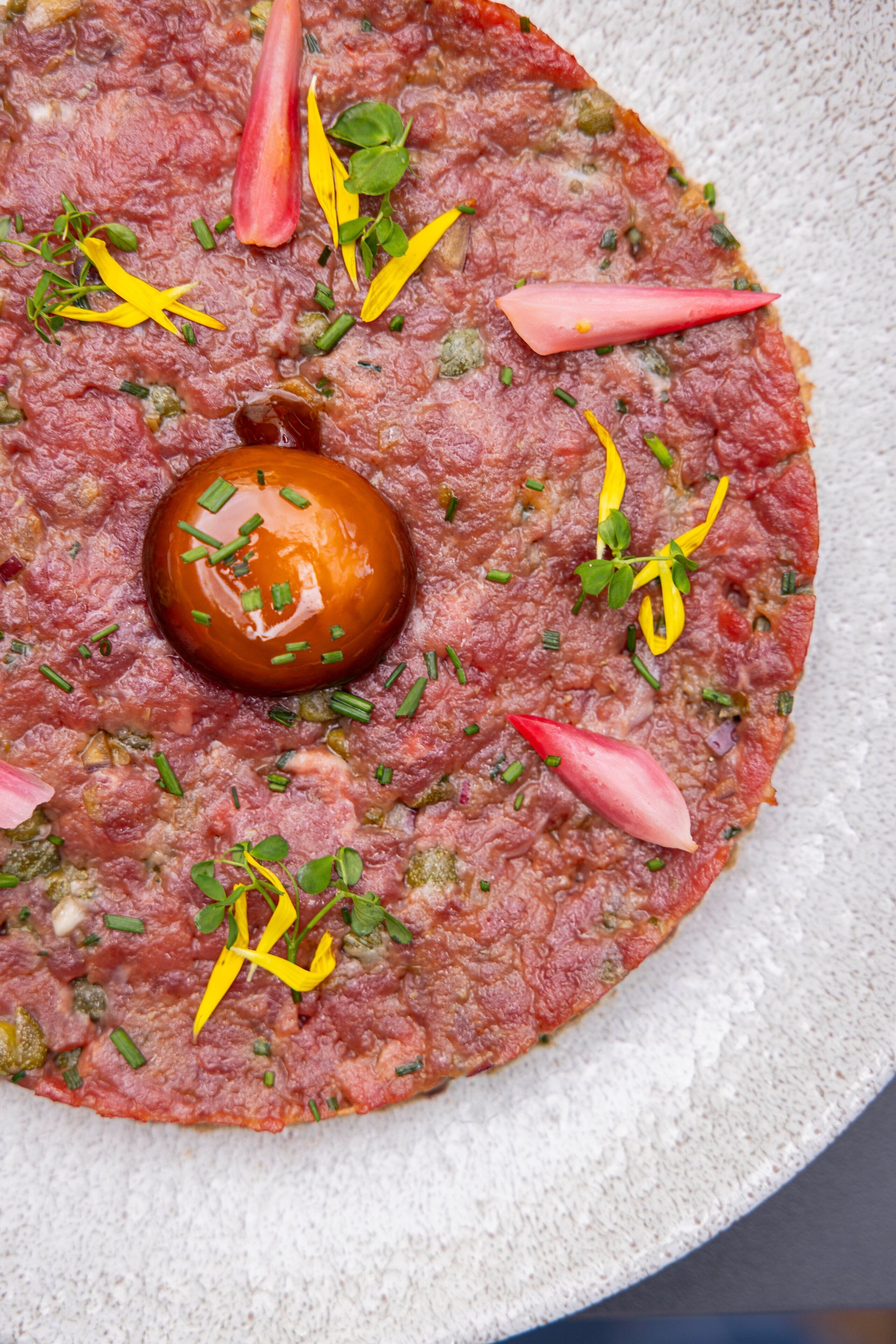 Un plato de carne redondo adornado con hierbas y un tomate cherry.