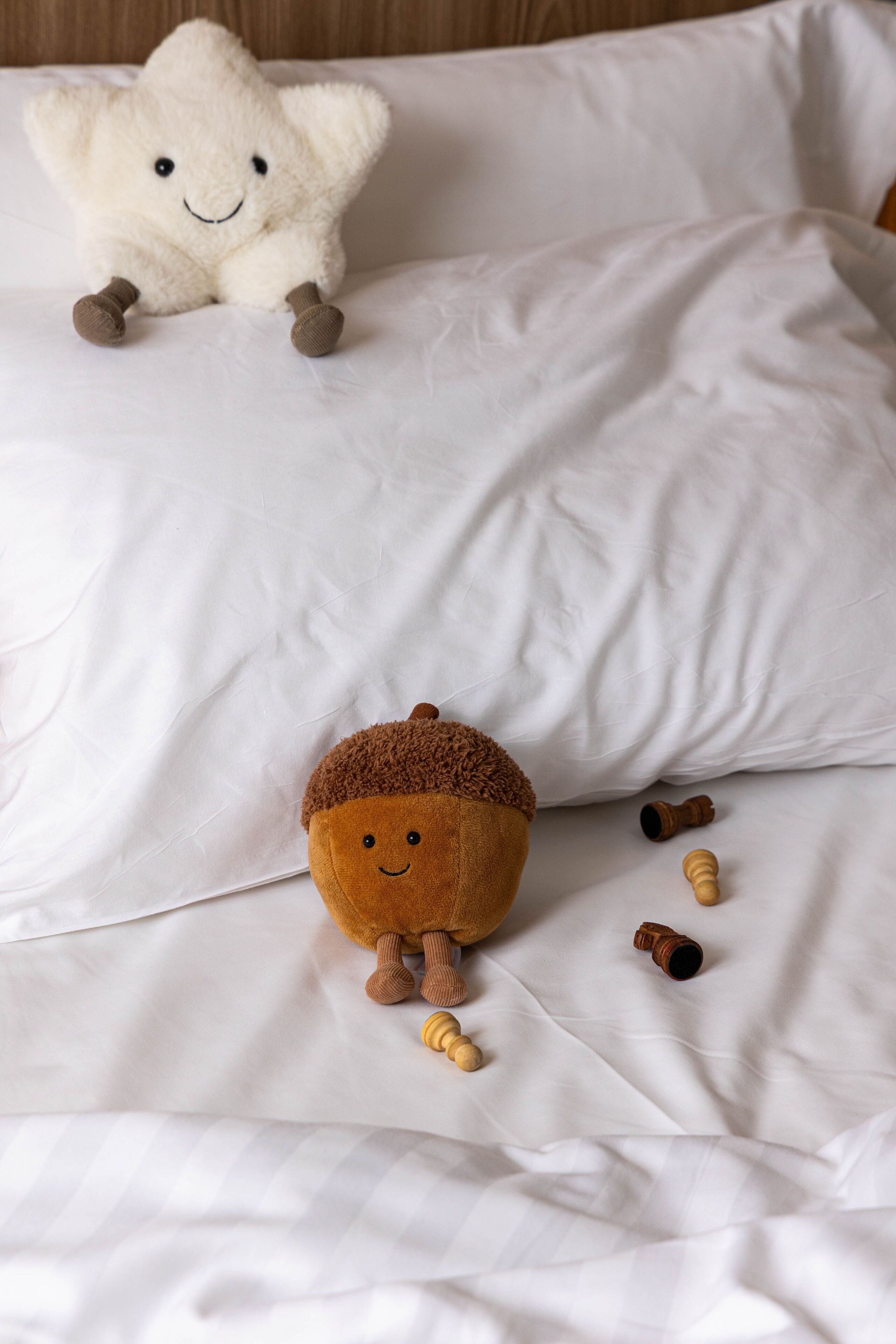 A bed with white sheets and pillows, a stuffed starfish, and a stuffed acorn toy.