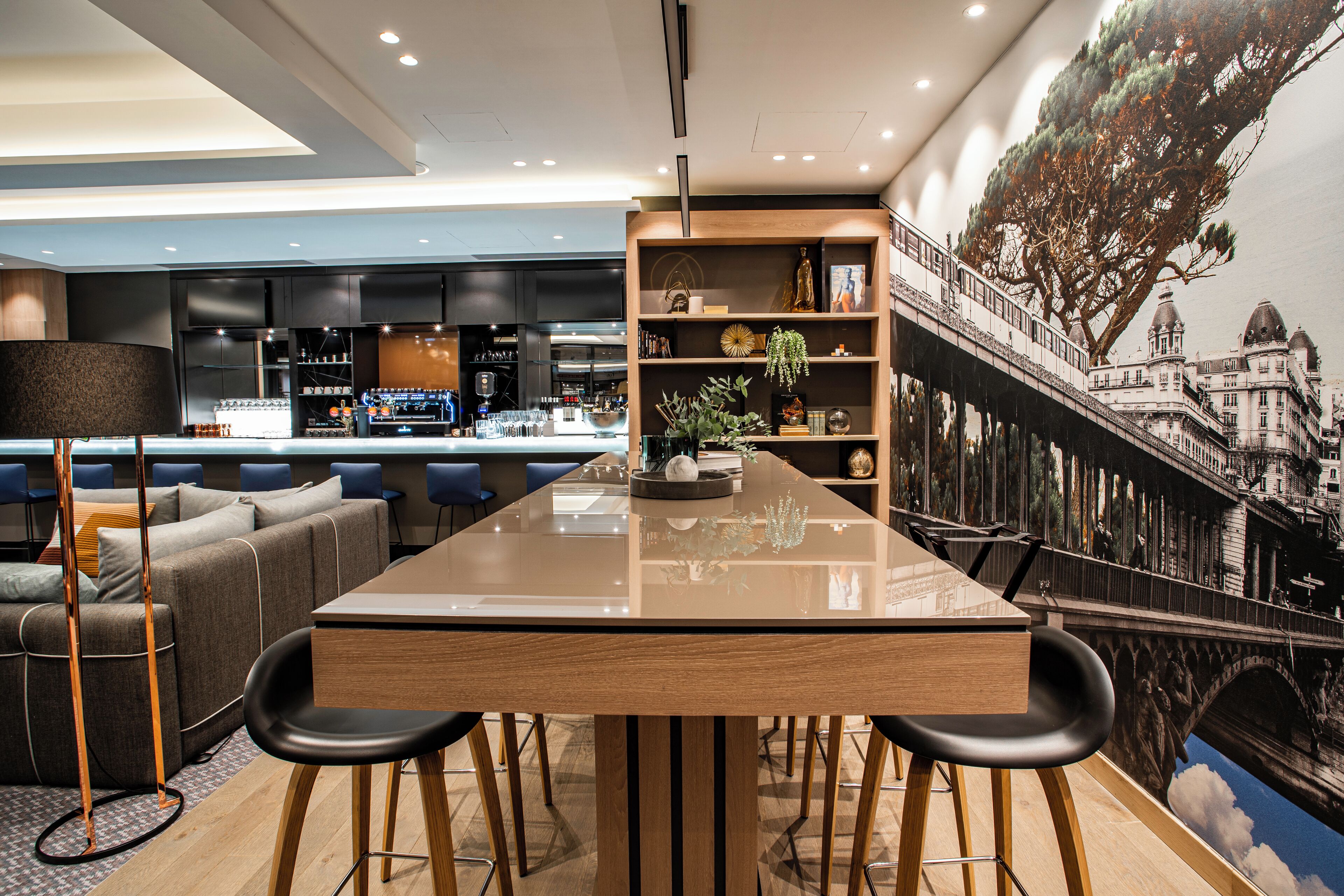 A modern interior with a dining area, a sofa, a bookshelf, and a mural of a bridge.