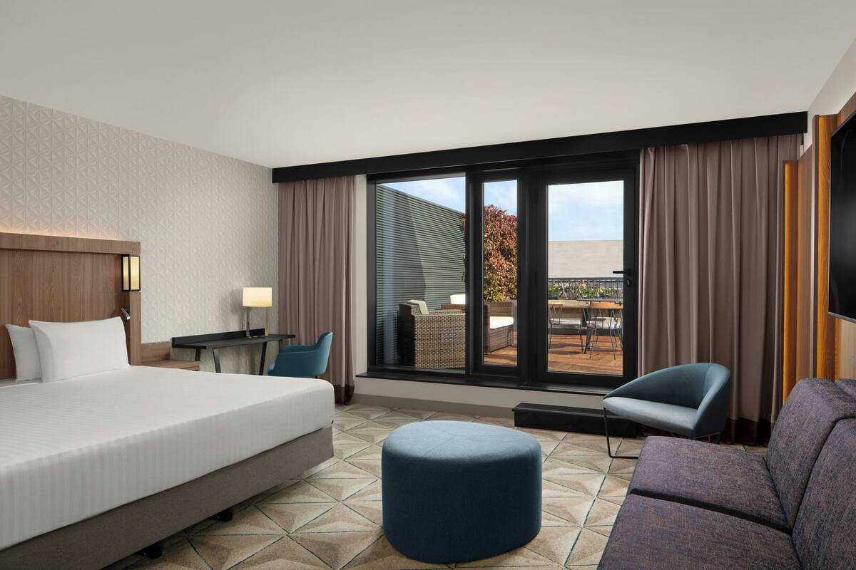 Hotelkamer met een bed, een bureau, een stoel, een bank en een groot raam met uitzicht op het landschap.