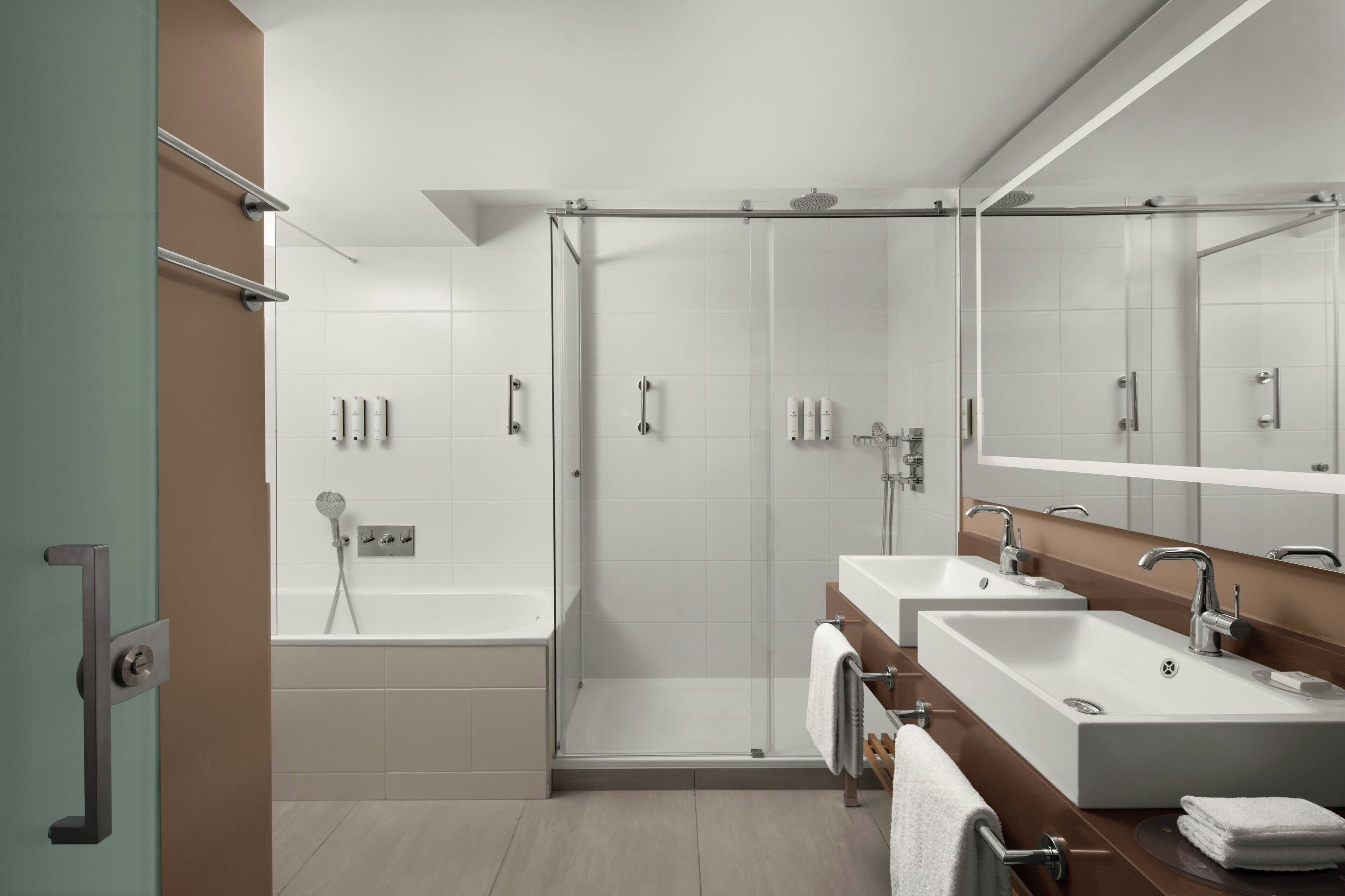 Ein modernes Badezimmer mit einer Glaskabine zur Dusche, einer Badewanne und zwei Waschbecken mit Spiegeln.