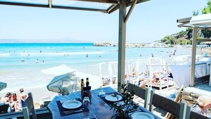 A beachside restaurant with outdoor seating overlooking the sea, featuring tables set for dining with bottles and glasses. - Villa Annie - Luxury Villa - 360 Sea & White Mountains views - Luxury hamper  (Tsivaras)