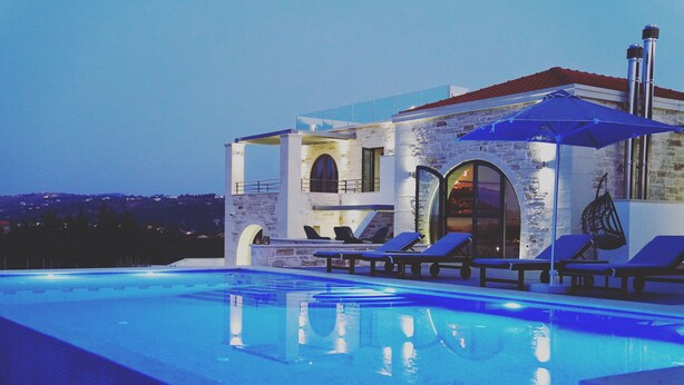 A modern poolside area with a clear view of the pool, lounge chairs, and a stone building with arched windows. - Villa Annie - Luxury Villa - 360 Sea & White Mountains views - Luxury hamper  (Tsivaras)