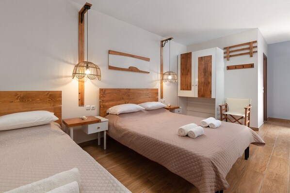 A modern hotel room with a wooden headboard, a large bed with a quilted bedspread, two bedside tables with lamps, a wooden wardrobe, and a chair.